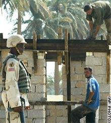 A U.S. soldier stands guard as two Iraqi contractors work on rebuilding a school at Jaafar al-Sakar, southwest of Baghdad.